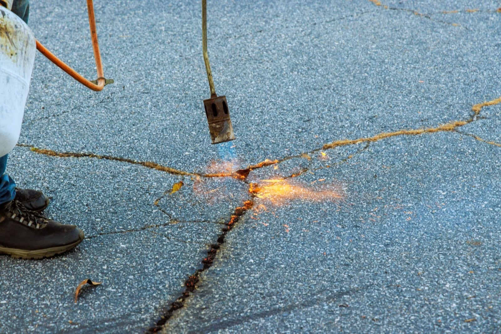 Worker burning dry grass from asphalt cracks during driveway restoration