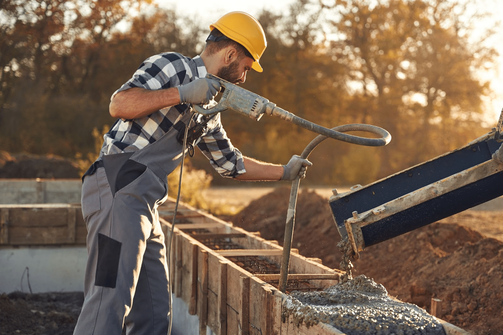 A construction worker pouring concrete into a home’s foundation at sunset.