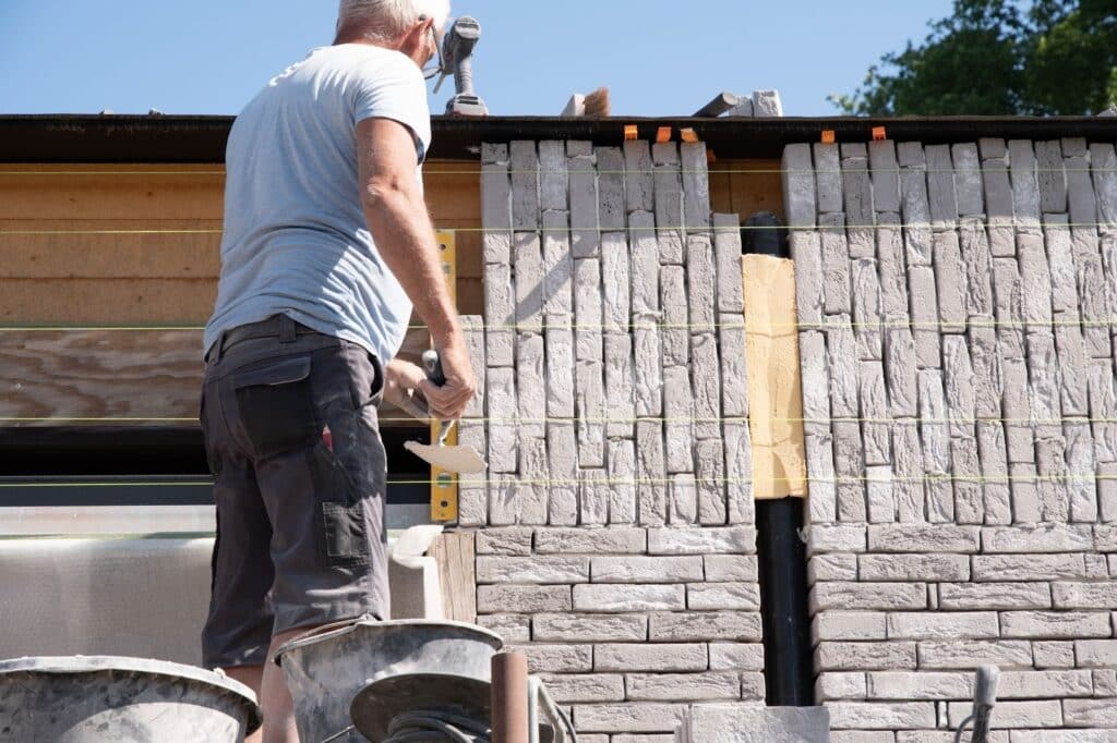 Professional masonry work showing a craftsman building a gray brick house facade with precision