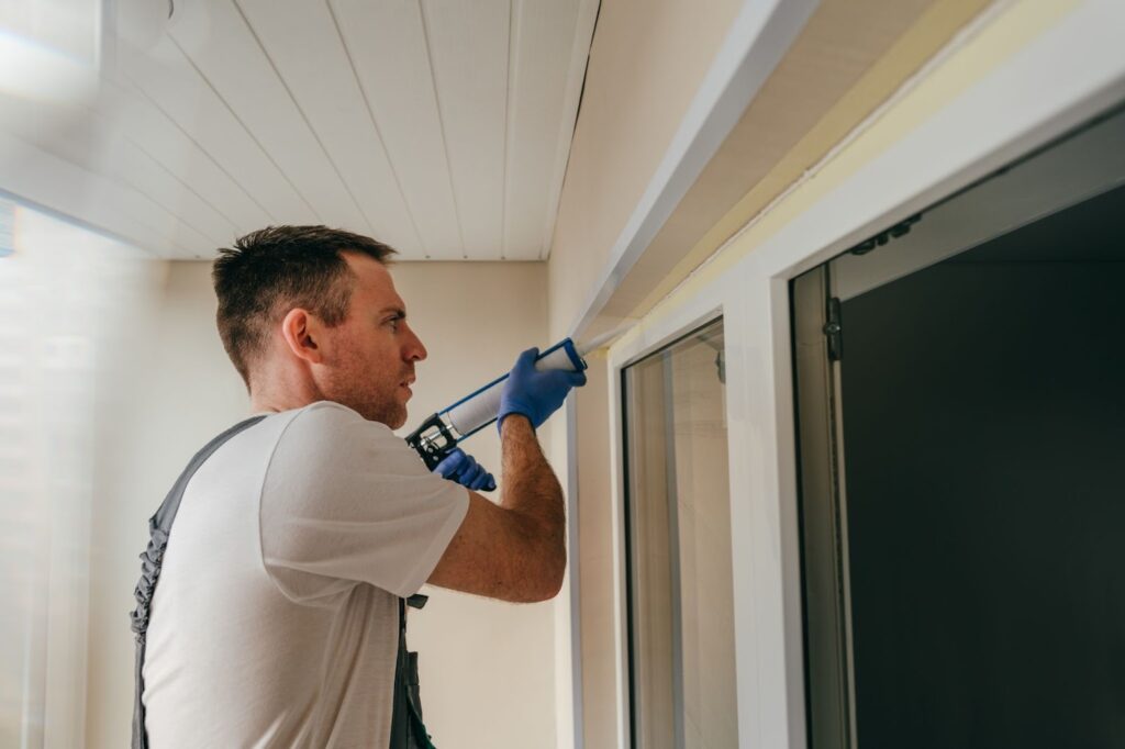 Worker in overalls applying caulking to seal cracks between the window frame and trim