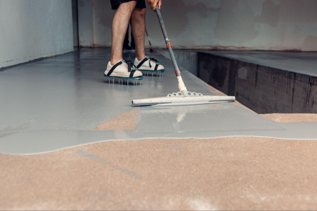 Cropped shot of a construction worker applying grey epoxy floor coating in a large industrial facility.